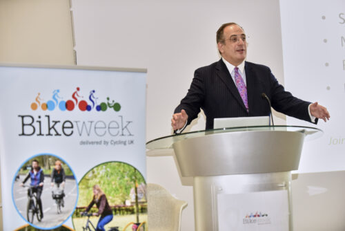 Cycling Minister Michael Ellis MP speaking at a lectern beside a Bike Week banner at the 2019 Parliamentary Bike Ride
