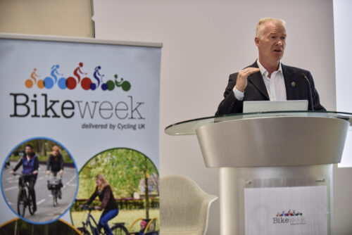 A man speaking at a lectern beside a Bike Week banner at the 2019 Parliamentary Bike Ride