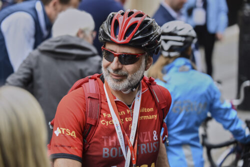 A smiling rider in a red helmet and sunglasses among cyclists on the 2019 Parliamentary Bike Ride