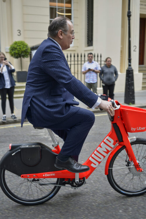 Cycling Minister Michael Ellis MP riding a red Jump hire bike in a suit