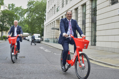 Cycling Minister Michael Ellis MP and another rider on red Jump hire bikes on a London street