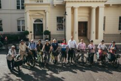 Riders lined up with their bikes in front of a white stucco terrace at the start of the 2023 Parliamentary Bike Ride