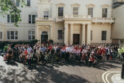 A large crowd of riders with their bikes outside a white stucco terrace at the start of the 2023 Parliamentary Bike Ride