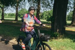 A woman in a bright patterned top riding a bike through a park on the 2023 Parliamentary Bike Ride
