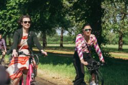 Two women in sunglasses cycling through a sunny park on the 2023 Parliamentary Bike Ride