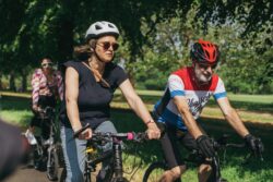 A woman and a man in helmets cycling through a park on the 2023 Parliamentary Bike Ride