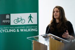 A woman speaking at a clear lectern in front of an All Party Parliamentary Group for Cycling & Walking banner