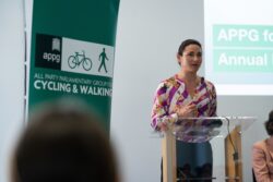 A woman speaking at a lectern beside an All Party Parliamentary Group for Cycling & Walking banner