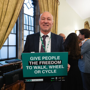 A smiling man holding a sign reading Give people the freedom to walk, wheel or cycle at the parliamentary reception