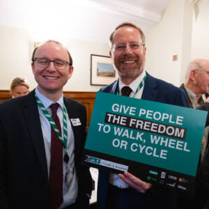 Two smiling men holding a sign reading Give people the freedom to walk, wheel or cycle at the parliamentary reception