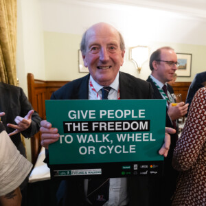 A smiling older man holding a Give people the freedom to walk, wheel or cycle sign at the parliamentary reception