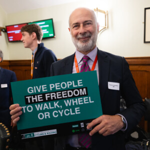 A man with a grey beard holding a Give people the freedom to walk, wheel or cycle sign at the parliamentary reception