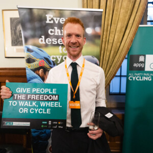 A man holding a Give people the freedom to walk, wheel or cycle sign beside an APPG for Cycling & Walking banner