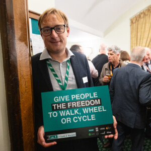 A man in glasses holding a Give people the freedom to walk, wheel or cycle sign at the parliamentary reception