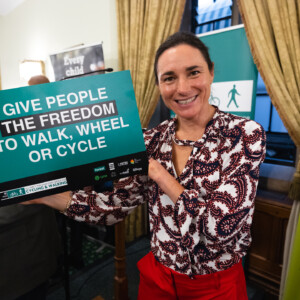 A smiling woman holding up a Give people the freedom to walk, wheel or cycle sign at the parliamentary reception
