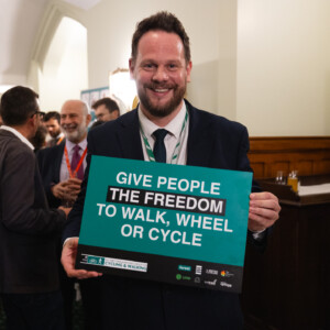 A smiling man holding a Give people the freedom to walk, wheel or cycle sign at the parliamentary reception