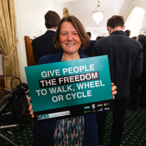 A smiling woman holding a Give people the freedom to walk, wheel or cycle sign at the parliamentary reception
