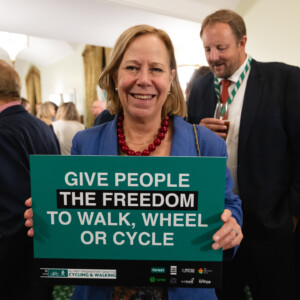 A smiling woman holding a Give people the freedom to walk, wheel or cycle sign at the parliamentary reception